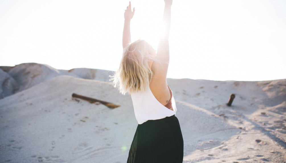 Woman raises her hands to the sun in happiness
