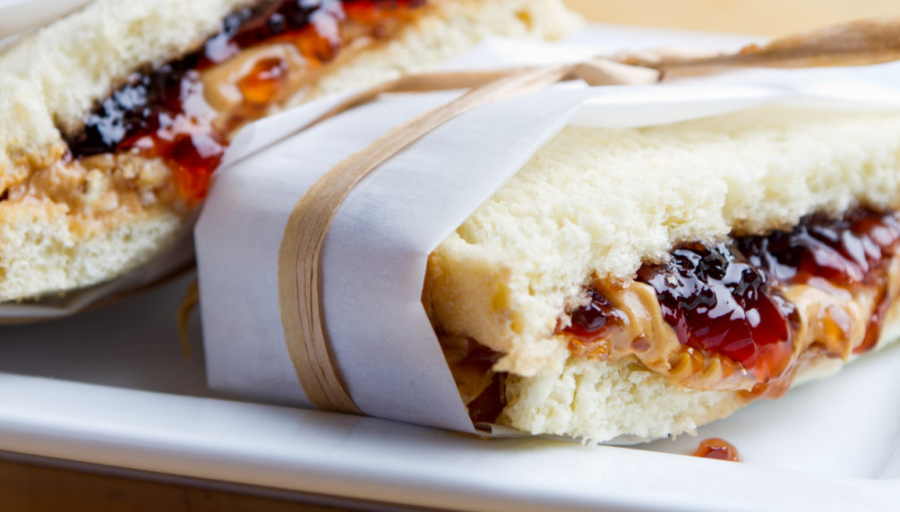 PB&J sandwich wrapped in parchment. Served on a white plate.