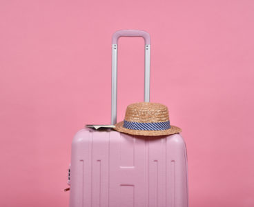 Pink suitcase and passport document over pink background