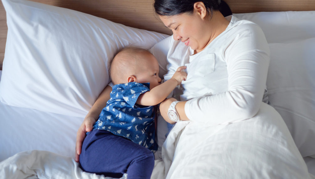 Asian mother is breastfeeding Cute little Asian 14 months / 1 year old toddler baby boy child in bed, Happy mom and smiling son looking at each other while breast feeding in bedroom at home