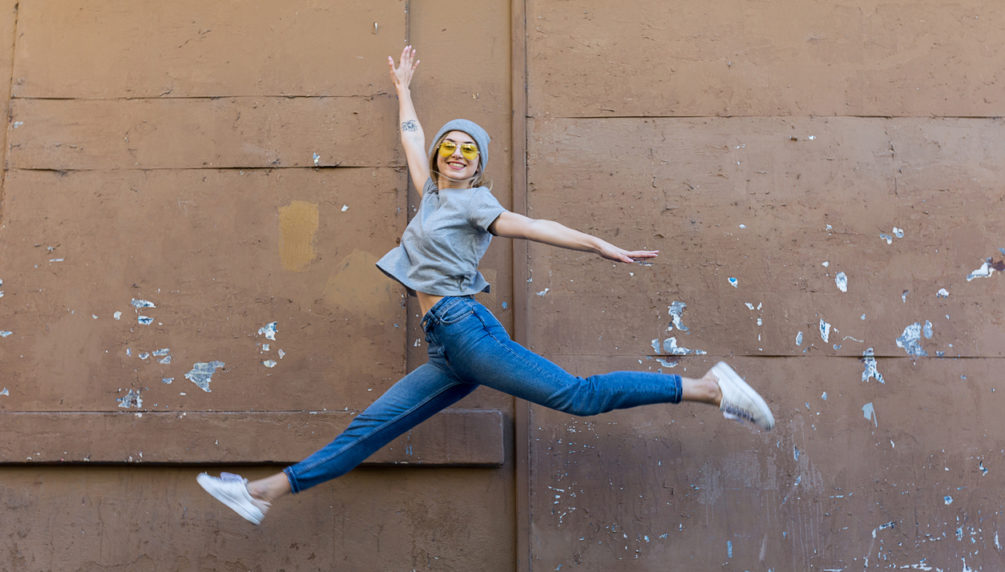 Young woman jumping front of wall