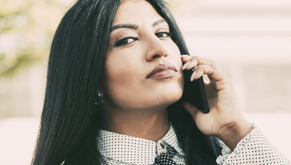 Arrogant confident businesswoman calling on phone and looking at camera. Serious young Hispanic female manager using mobile phone to connect client. Communication concept